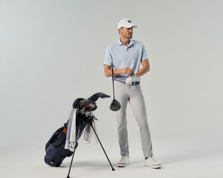 Man holding a golf club next to a golf bag on a gray background